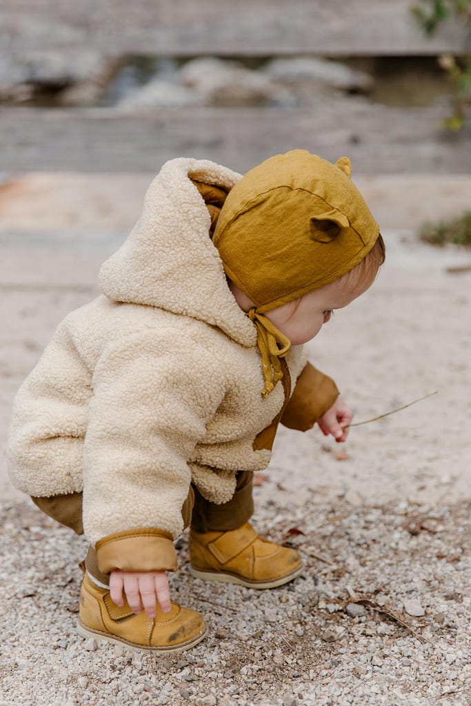 Un bébé mignon portant un manteau d'hiver et un chapeau explore les galets à l'extérieur.